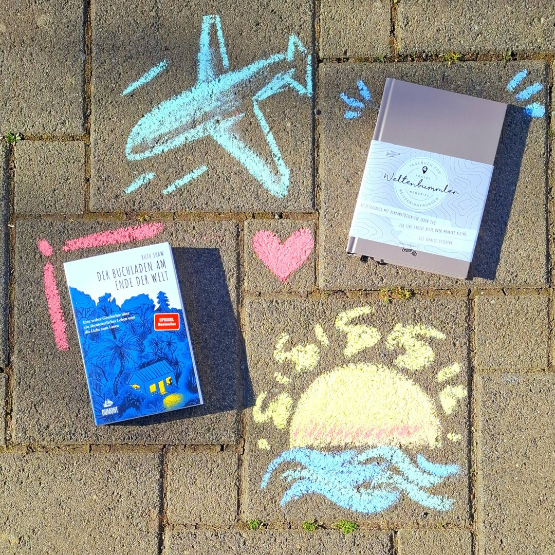 Aus der Vogelperspektive sind die beiden B&uuml;cher "Weltenbummler" und "Der Buchladen am Ende der Welt" neben einem Flugzeug und einer Sonne gemalt mit Kreide zu sehen.